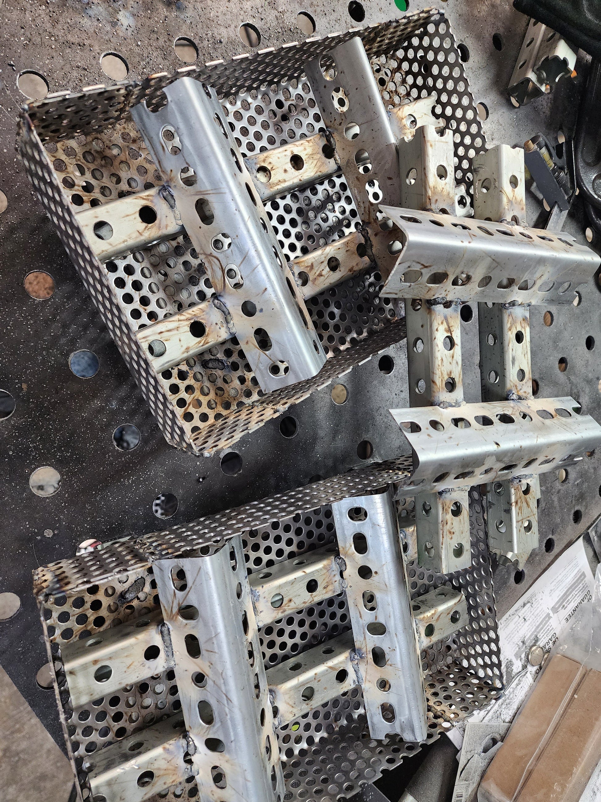 Two perforated metal baskets with three Square tube and angle iron wood pellet inserts arranged on a welding table