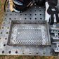 One large perforated steel basket and one square tube and angle iron wood pellet insert on a welding table