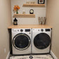Custom butcher block countertop over front-loading washer and dryer, with two wooden shelves in a compact laundry room setup.