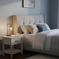 Barnwood nightstand with a drawer and lower storage shelf beside a beige upholstered bed in a blue-gray farmhouse bedroom