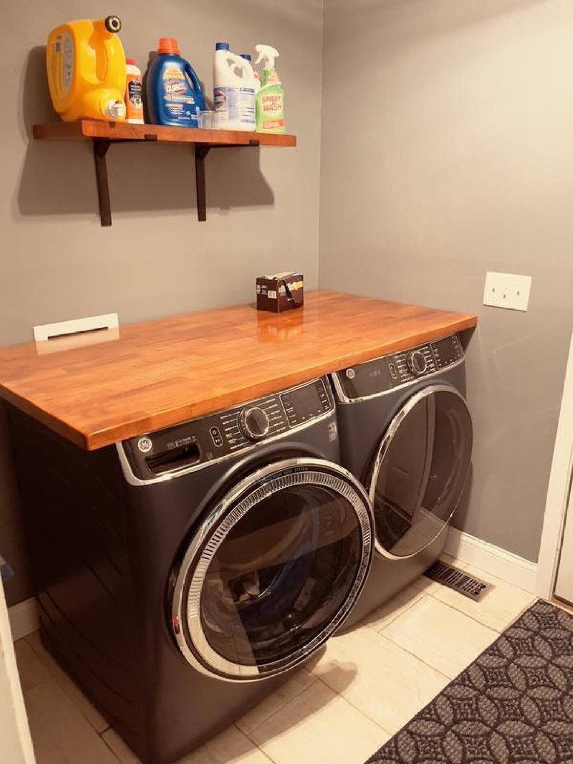 Butcher block countertop for laundry room folding and utility upgrade over front-loading washer and dryer, with a wall shelf holding cleaning supplies.