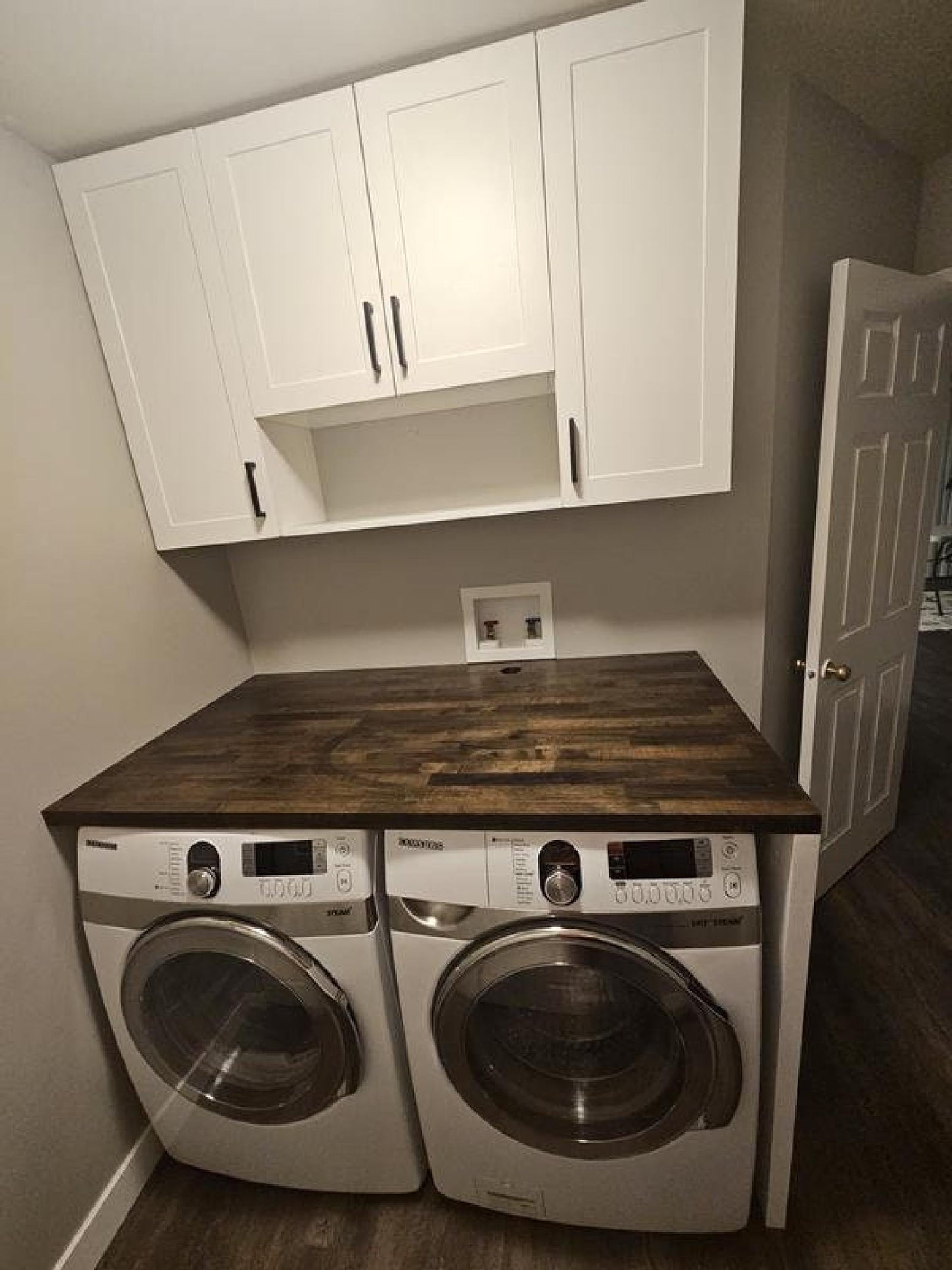 Custom butcher block countertop for laundry room over front-load washer and dryer, dark wood with white cabinets.