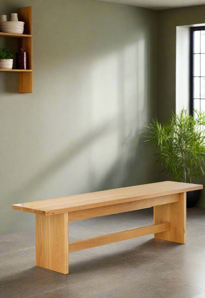 A white oak wood bench with a cushion on it, placed against a light blue wall on a hardwood floor.